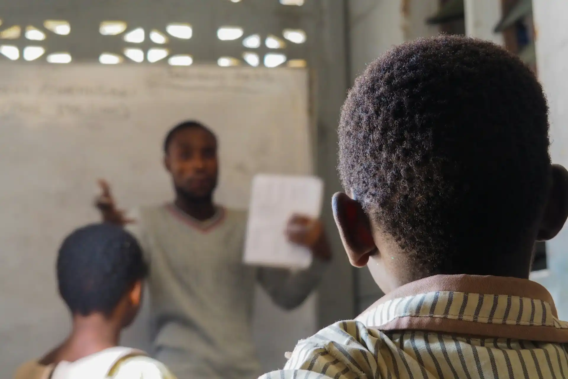 A teacher at a chalkboard and a young student holding a book